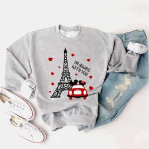 May include: Gray sweatshirt with a black and white illustration of the Eiffel Tower, a red car with Mickey and Minnie Mouse inside, and the text "I'm always with you". There are red hearts scattered around the design.