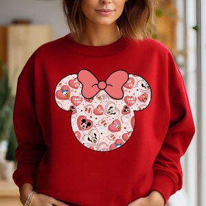 May include: Red sweatshirt with a pink and white Mickey Mouse ears design. The ears are filled with hearts and characters from Disney.