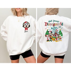 Op de afbeelding: Witte sweatshirt met Mickey Mouse in een kerstkrans en de naam "Jeff" eronder. De achterkant toont een kleurrijke afbeelding van Disney-personages en de tekst "Walt Disney's Disneyworld 1971".