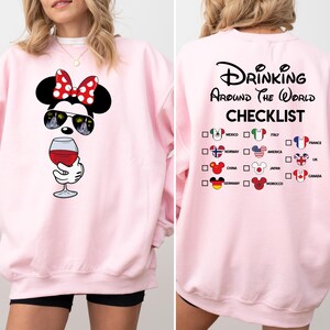 Puede incluir: Sudadera rosa con un dise&ntilde;o de Mickey Mouse bebiendo vino. La parte posterior de la sudadera tiene una lista de verificaci&oacute;n de pa&iacute;ses con banderas y el texto "Drinking Around the World Checklist".