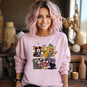 Puede incluir: Sudadera rosa claro con un gr&aacute;fico de Halloween con personajes de dibujos animados. El gr&aacute;fico incluye a Mickey Mouse, Minnie Mouse, Donald Duck y Goofy con disfraces de Halloween. La sudadera tiene mangas largas.