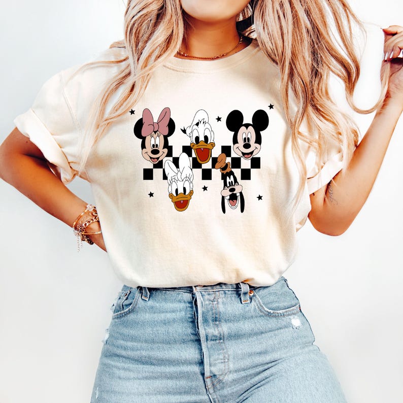 Puede incluir: Una camiseta blanca con un patr&oacute;n de cuadros blanco y negro e im&aacute;genes de Mickey Mouse, Minnie Mouse, Donald Duck y Goofy. Los personajes sonr&iacute;en y tienen contornos negros.