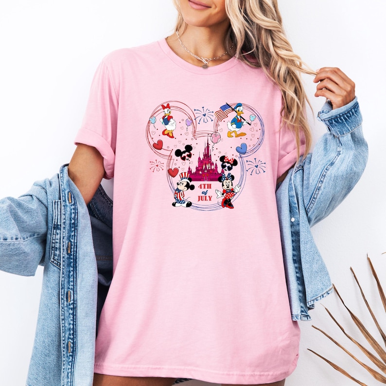 Peut inclure: T-shirt rose clair avec un motif patriotique mettant en vedette des personnages Disney. Le motif comprend Mickey et Minnie Mouse, Donald et Daisy Duck, un ch&acirc;teau, des feux d'artifice, des c&oelig;urs et le texte "4th of July". Le t-shirt a un col rond et des manches courtes.