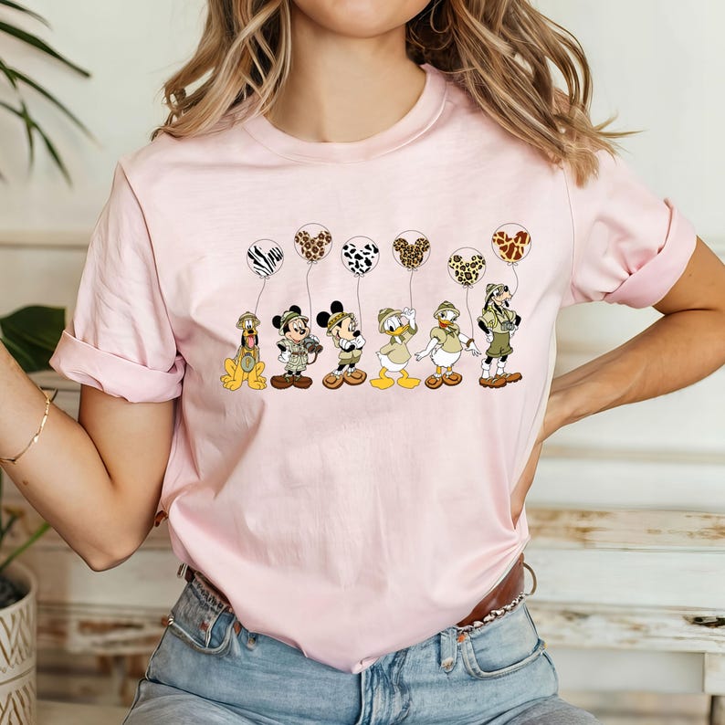 Pode incluir: Camiseta rosa com um gr&aacute;fico de Mickey Mouse, Donald Duck, Pateta e Pluto vestidos com roupas de saf&aacute;ri segurando bal&otilde;es com estampa de animais.