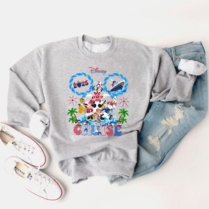 May include: A gray Disney Cruise sweatshirt featuring Mickey Mouse and friends. The design includes the word "Cruise" and the year "2025". The sweatshirt is paired with blue jeans and white sneakers.