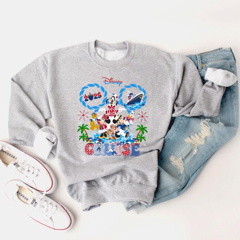 May include: A gray Disney Cruise sweatshirt featuring Mickey Mouse and friends. The design includes the word "Cruise" and the year "2025". The sweatshirt is paired with blue jeans and white sneakers.