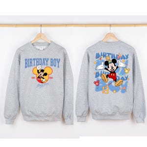 May include: Grey sweatshirt with a Mickey Mouse graphic on the front. The front graphic says "Birthday Boy" with "Est. 2011" and "Mickey Mouse" underneath. The back of the sweatshirt has a larger Mickey Mouse graphic with the words "Birthday Boy" and the number "13" in blue.