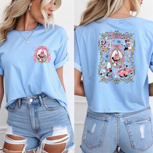 May include: A light blue t-shirt with a graphic of Mickey Mouse and friends in front of a pink castle on the front and the word "Bestie" with a graphic of Mickey Mouse and friends on the back.