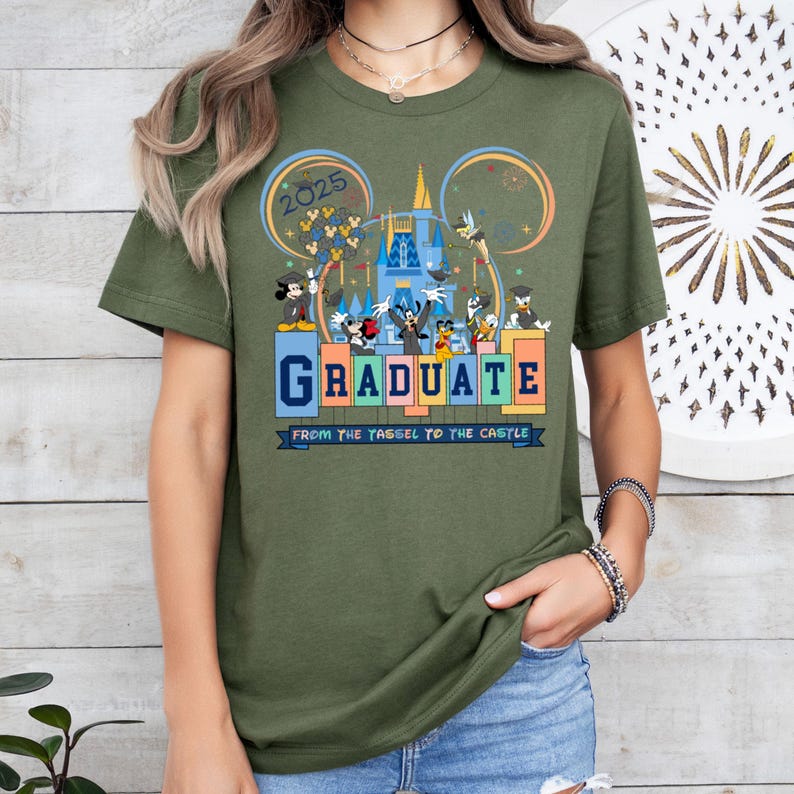 May include: Green t-shirt with a graphic of Mickey Mouse and friends celebrating graduation at Disney World. The text on the shirt reads "2025 Graduate From the Tassel to the Castle".