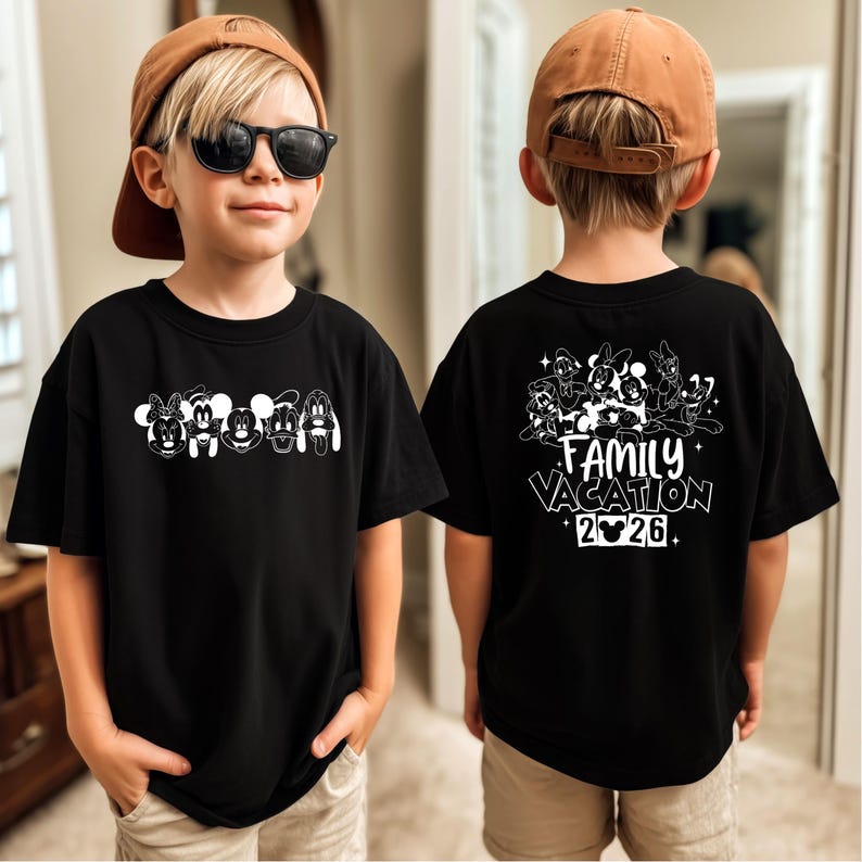 May include: Black t-shirt featuring white cartoon character faces across the front. The back of the shirt displays a group of cartoon characters with the words "Family Vacation 2026". The shirt is worn by a child.