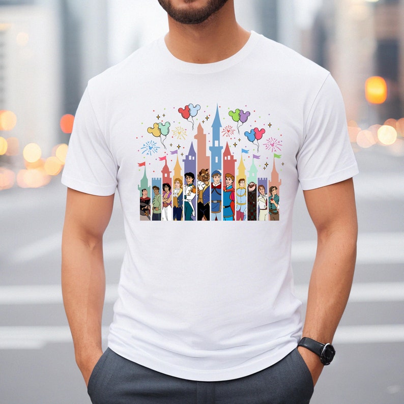 Puede incluir: Camiseta blanca con una ilustraci&oacute;n colorida del castillo de Disney y los pr&iacute;ncipes. El castillo est&aacute; rodeado de globos y fuegos artificiales.