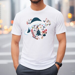 May include: White t-shirt featuring a Christmas-themed design. The graphic includes a blue and white Santa hat shape filled with Christmas elements like a tree, gifts, and candy canes. The shirt has short sleeves and a crew neck.
