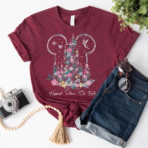 May include: A maroon t-shirt with a floral design of a castle in the shape of Mickey Mouse ears. The text "Happiest Place On Earth" is printed below the castle.