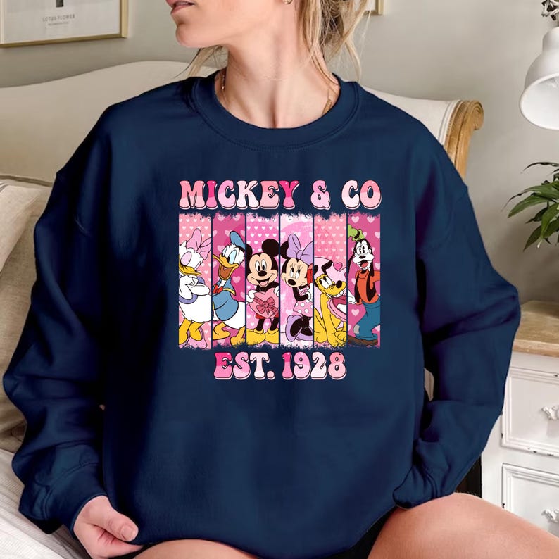 Puede incluir: Sudadera azul marino con un gr&aacute;fico rosa y blanco de Mickey Mouse y sus amigos. El gr&aacute;fico incluye el texto "Mickey & Co. Est. 1928".