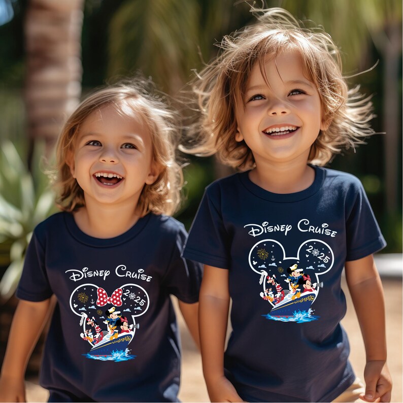 May include: Two children wearing navy blue t-shirts with a Disney Cruise design. The design features Mickey Mouse ears, fireworks, and the text "Disney Cruise 2025". The children are smiling and holding hands, suggesting a joyful occasion.