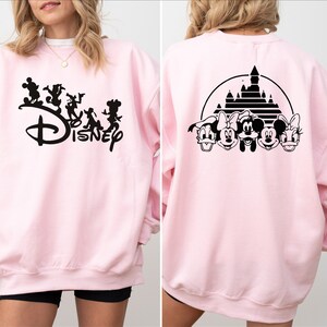 Puede incluir: Sudadera rosa con un gr&aacute;fico negro de Mickey Mouse y sus amigos caminando frente al logotipo de Disney en la parte delantera. La parte posterior de la sudadera tiene un gr&aacute;fico negro de Mickey Mouse y sus amigos frente al castillo de Disney.