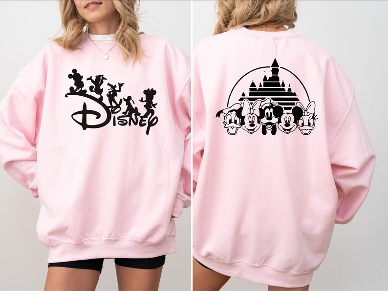 Puede incluir: Sudadera rosa con un gr&aacute;fico negro de Mickey Mouse y sus amigos caminando frente al logotipo de Disney en la parte delantera. La parte posterior de la sudadera tiene un gr&aacute;fico negro de Mickey Mouse y sus amigos frente al castillo de Disney.