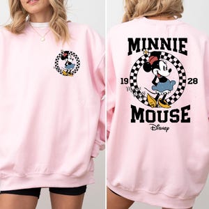 May include: Pink sweatshirt with a black and white checkered graphic featuring Minnie Mouse and the text "Minnie Mouse Disney" on the back. The front of the sweatshirt has a small graphic of Minnie Mouse.