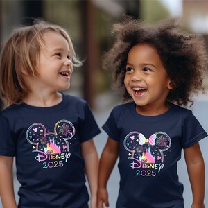 May include: Two children wearing navy blue t-shirts with a colorful Disney castle graphic and the text "DISNEY 2025". One shirt features Mickey Mouse ears and the other features Minnie Mouse ears.