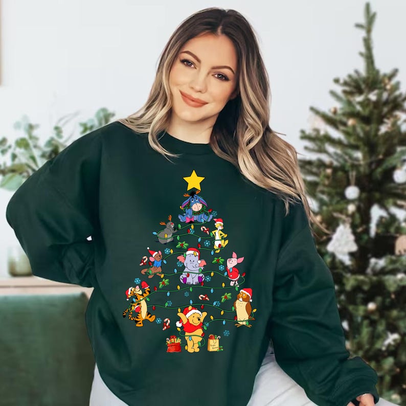 Pu&ograve; includere: Una felpa verde scuro con un design ad albero di Natale composto da personaggi dei cartoni animati. L'albero &egrave; decorato con luci, ornamenti e una stella gialla. I personaggi includono Winnie the Pooh, Tigro, Pimpi ed Eeyore.