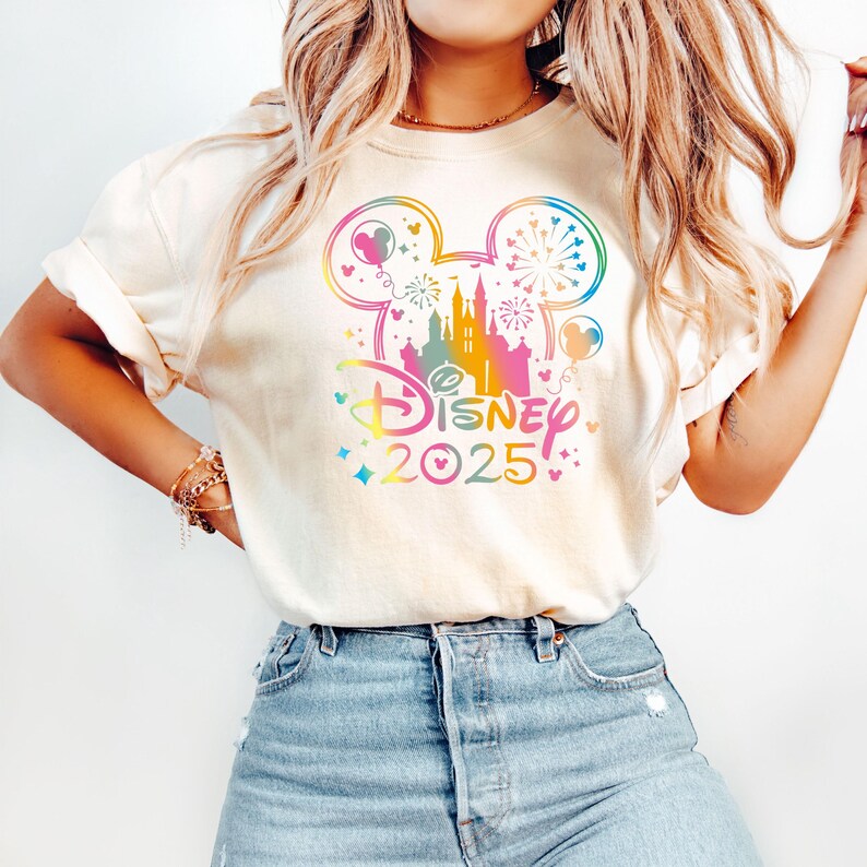 May include: A white t-shirt with a rainbow-colored Mickey Mouse silhouette and the text "DISNEY 2025" printed on the front.