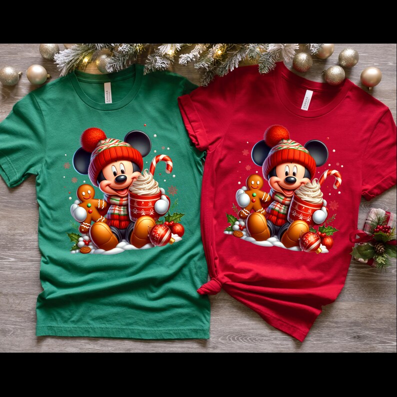 May include: Two Christmas themed t-shirts featuring a cartoon Mickey Mouse wearing a Santa hat and holding a cup of hot chocolate. One shirt is green and the other is red.