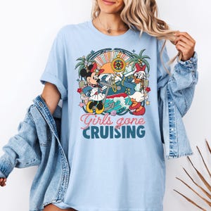 May include: Light blue t-shirt with a graphic of Minnie Mouse and Daisy Duck dressed as sailors on a boat. The text "Girls gone cruising" is printed below the graphic.