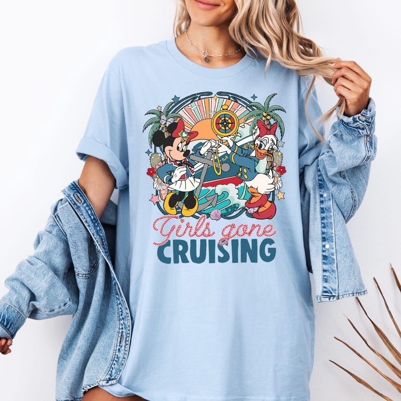 May include: Light blue t-shirt with a graphic of Minnie Mouse and Daisy Duck dressed as sailors on a boat. The text "Girls gone cruising" is printed below the graphic.