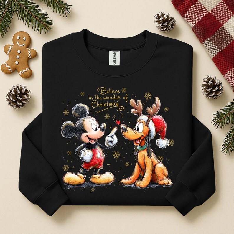May include: Black sweatshirt featuring Mickey Mouse and Pluto with Christmas-themed designs. Mickey Mouse is wearing red shorts and Pluto is wearing a Santa hat. The text "Believe in the wonder of Christmas" is displayed in gold.