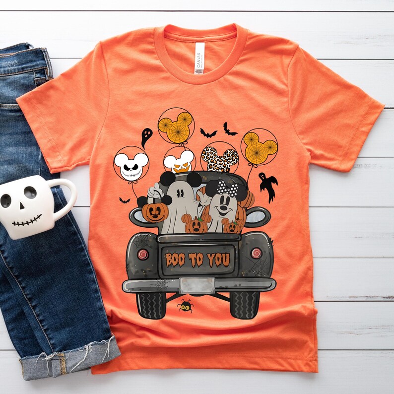 Peut inclure: T-shirt orange avec une illustration en noir et blanc de Mickey Mouse, Minnie Mouse et un fant&ocirc;me dans un pick-up noir avec des citrouilles. Le camion porte l'inscription "Boo to You" &agrave; l'arri&egrave;re.