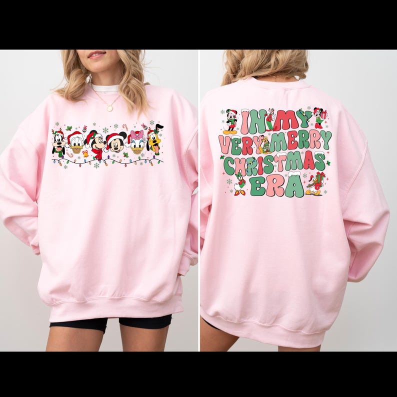 May include: Pink sweatshirt with a Christmas design featuring Mickey Mouse and friends on the front and the text "In My Very Merry Christmas Era" on the back.