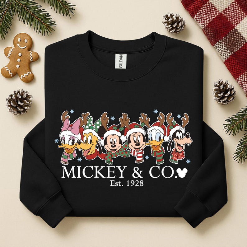 K&ouml;nnte beinhalten: Schwarzes Sweatshirt mit Disney-Figuren als Rentiere mit Geweihen und Schals. Mickey, Minnie, Donald, Daisy, Goofy und Pluto sind abgebildet. Der Text "Mickey & Co. Est. 1928" ist darunter gedruckt.