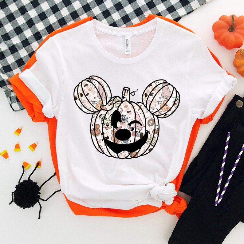 Op de afbeelding: Wit T-shirt met een zwart-wit Mickey Mouse pompoenontwerp. De pompoen is gemaakt van verschillende Halloween-afbeeldingen.
