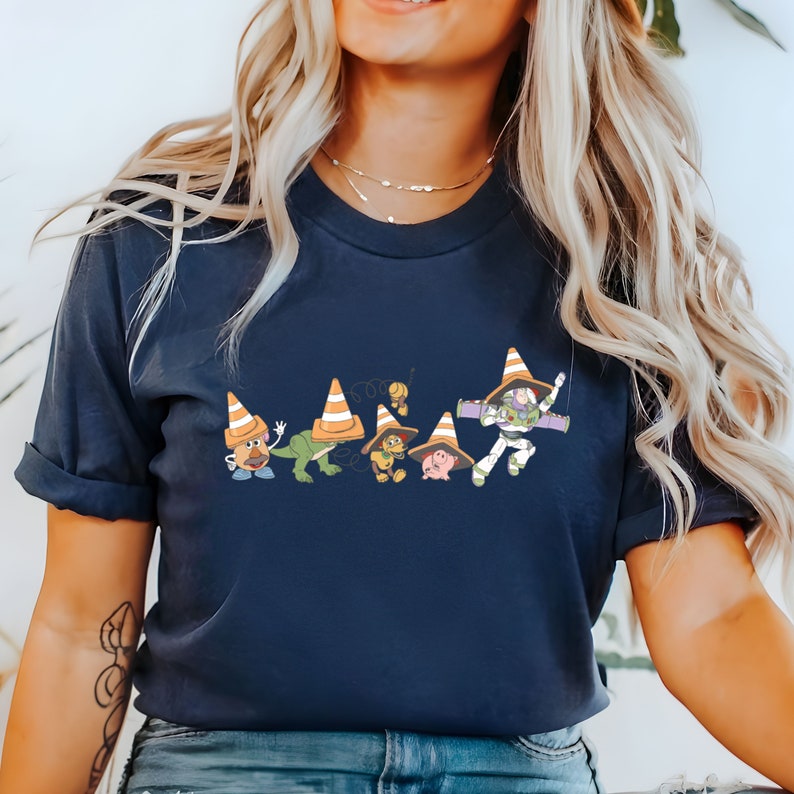 Op de afbeelding: Een donkerblauw T-shirt met een afbeelding van de Toy Story-personages die verkeerskegels dragen. De personages zijn Woody, Buzz Lightyear, Mr. Potato Head, Rex, Slinky Dog en Hamm.