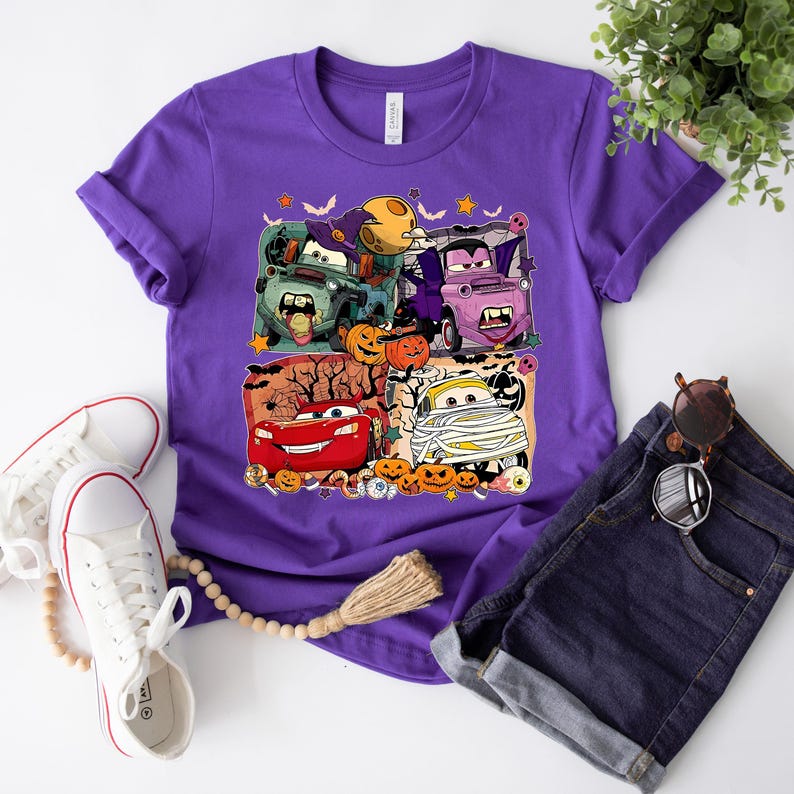 May include: Purple t-shirt with a Halloween-themed graphic featuring characters from the Cars movie franchise. The graphic includes Lightning McQueen, Mater, and other characters dressed in costumes.