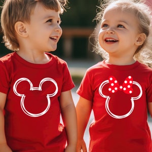 May include: Two children wearing red t-shirts with white Mickey Mouse and Minnie Mouse silhouettes. The girl's shirt has a red polka dot bow on Minnie Mouse's head.