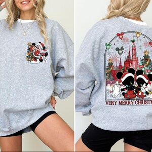 May include: Gray sweatshirt with a Christmas theme featuring Mickey Mouse and Minnie Mouse in front of a castle with the text "Very Merry Christmas".