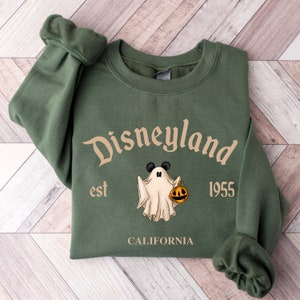 Puede incluir: Sudadera verde con un fantasma blanco que sostiene una calabaza. El texto "Disneyland est 1955 CALIFORNIA" est&aacute; impreso en la parte delantera.
