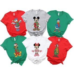 May include: A collection of six short-sleeved t-shirts in various colors, each featuring a different Disney character in festive holiday attire. Characters include Mickey, Minnie, Donald, Daisy, Goofy, and Pluto, all adorned with Christmas lights.