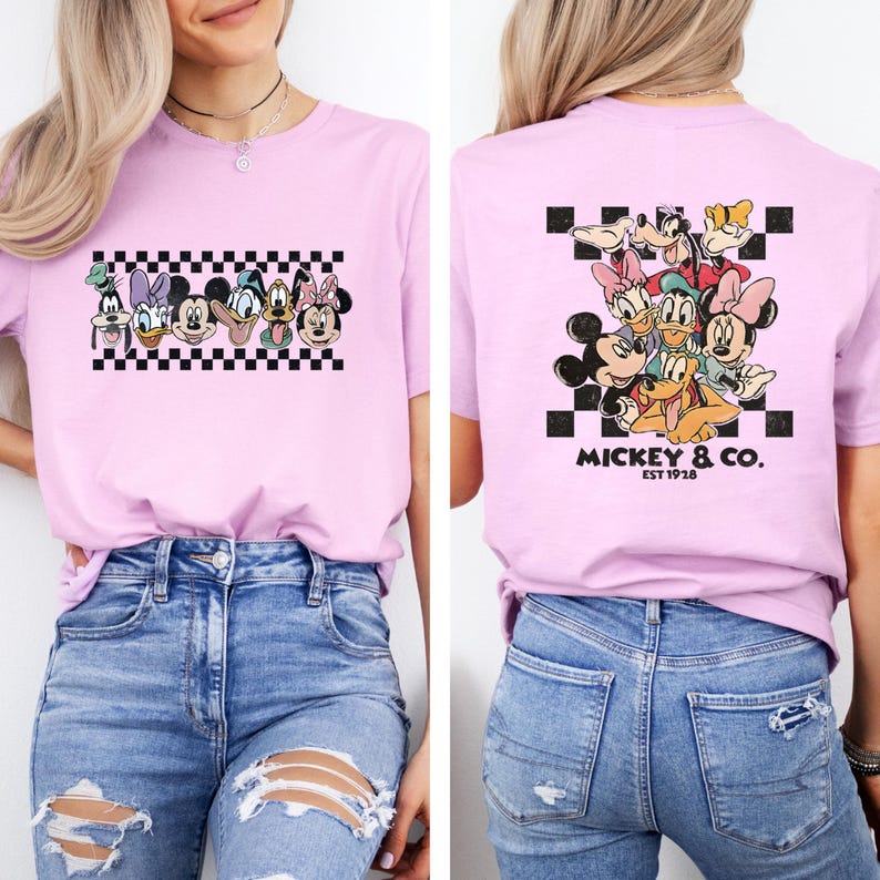 May include: A light pink t-shirt featuring a graphic of Disney characters on the front and back. The front design includes Mickey, Minnie, Donald, Daisy, and Goofy above a black and white checkered pattern. The back design features the same characters with the text "Mickey & Co. EST 1928".