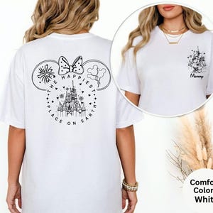 May include: White t-shirt with a black graphic on the back featuring a castle, fireworks, and the text "THE HAPPIEST PLACE ON EARTH." The front of the shirt has a smaller graphic with the word "Mommy."