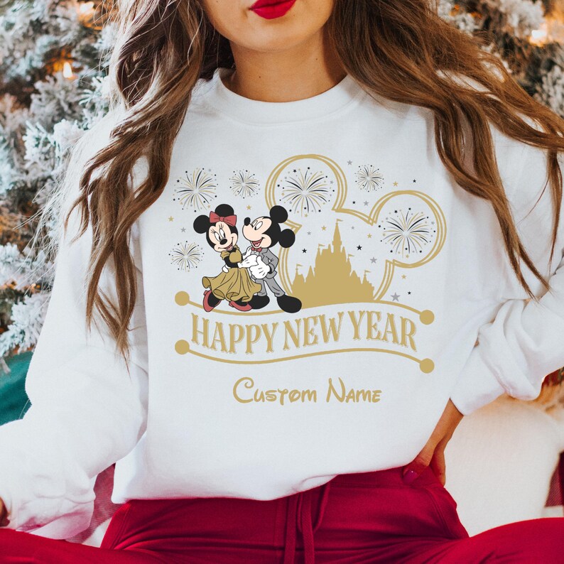 May include: White sweatshirt with a gold design featuring Mickey and Minnie Mouse in front of Cinderella's Castle. The design includes fireworks and the text "Happy New Year" and "Custom Name".