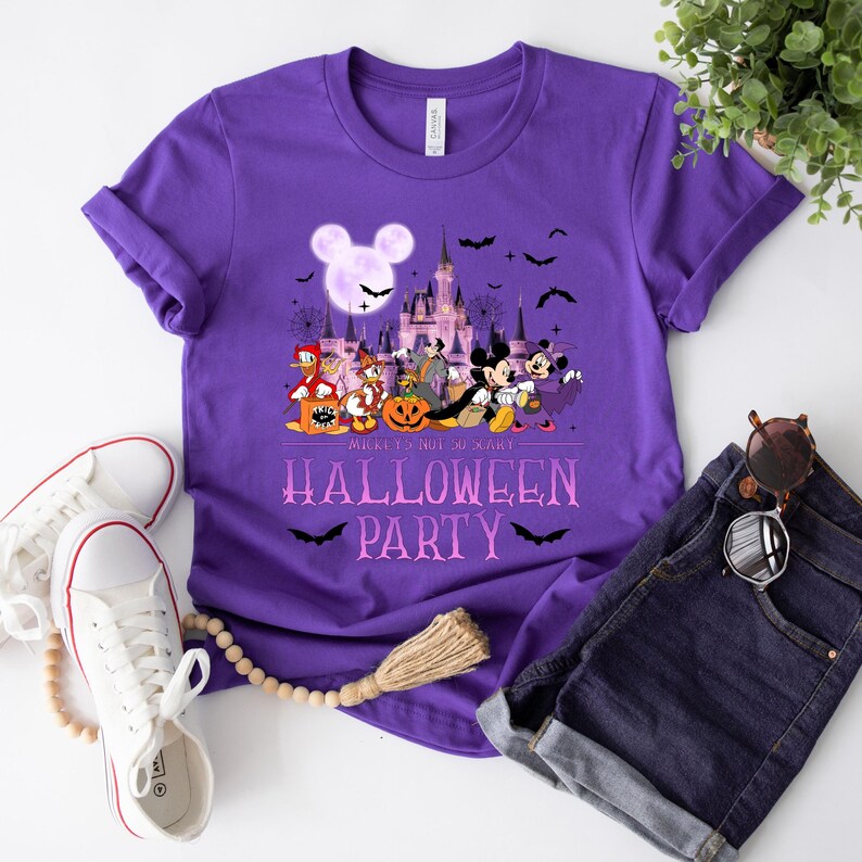 Puede incluir: Camiseta morada con un gr&aacute;fico de Mickey Mouse y sus amigos disfrazados para Halloween frente al Castillo de Cenicienta. El texto "Mickey's Not So Scary Halloween Party" est&aacute; impreso en la camiseta.