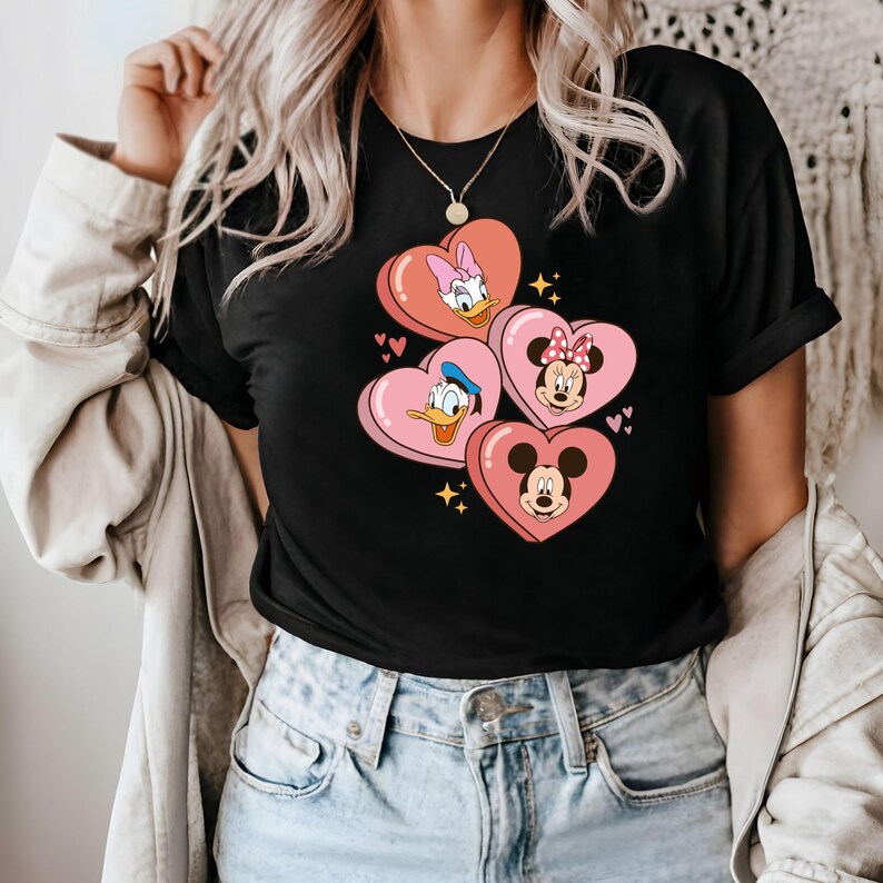 Puede incluir: Camiseta negra con un gr&aacute;fico de Mickey Mouse, Minnie Mouse, Donald Duck y Daisy Duck en corazones rosas.