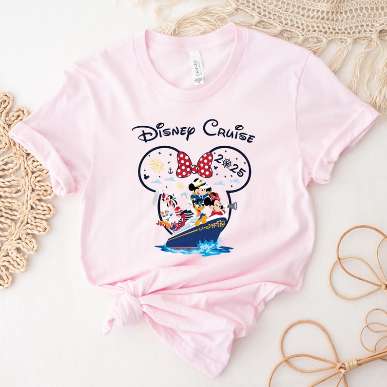 May include: A light pink t-shirt featuring the words "Disney Cruise" above a graphic of Mickey and Minnie Mouse, Donald Duck, and Goofy on a cruise ship. The graphic includes the year "2025".