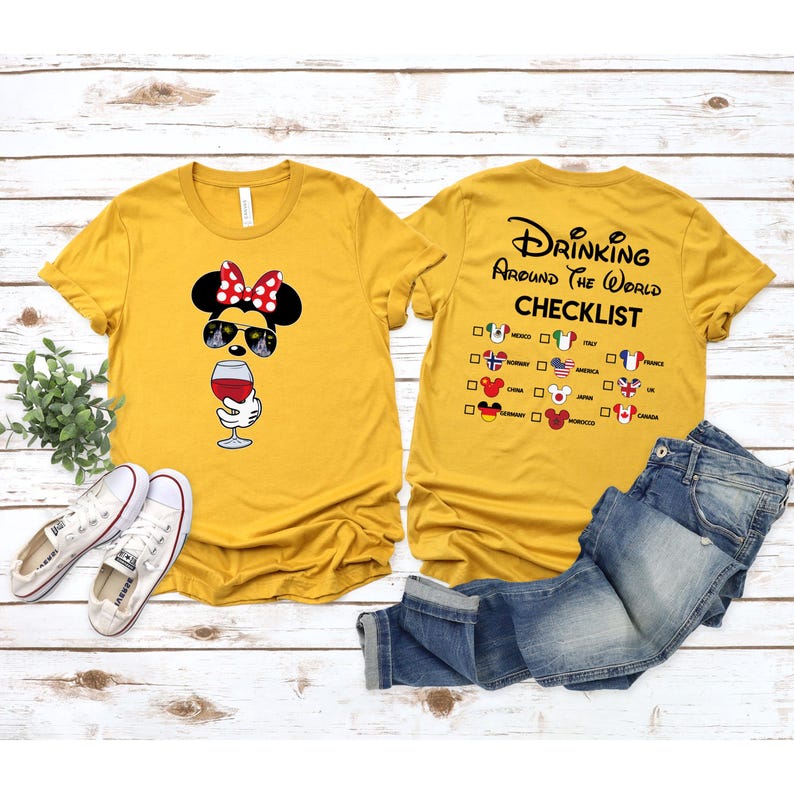 Puede incluir: Dos camisetas amarillas con un dise&ntilde;o de tem&aacute;tica Disney. Una camiseta presenta una imagen de dibujos animados de Minnie Mouse con gafas de sol y sosteniendo una copa de vino. La otra camiseta tiene el texto "Drinking Around the World Checklist" con una lista de pa&iacute;ses y banderas.