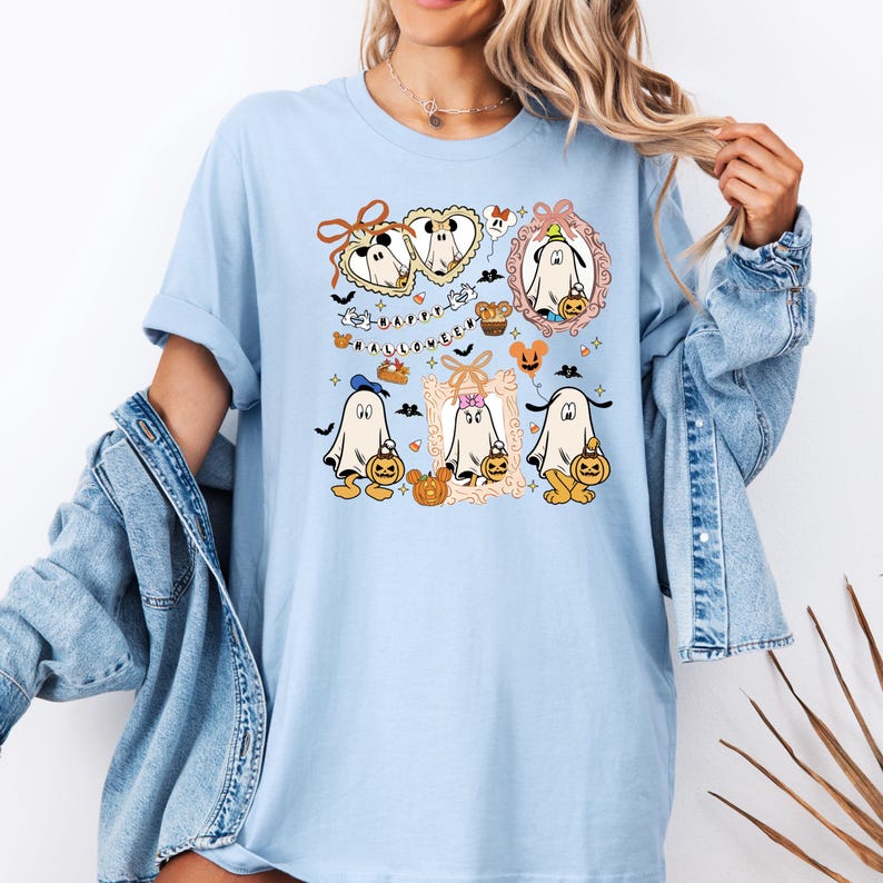 Puede incluir: Camiseta azul claro con un dise&ntilde;o de Halloween. El dise&ntilde;o incluye fantasmas de dibujos animados sosteniendo calabazas, enmarcados en bordes ornamentados, con el texto "HAPPY HALLOWEEN" en una fuente juguetona. La camiseta tiene mangas cortas y un corte holgado.