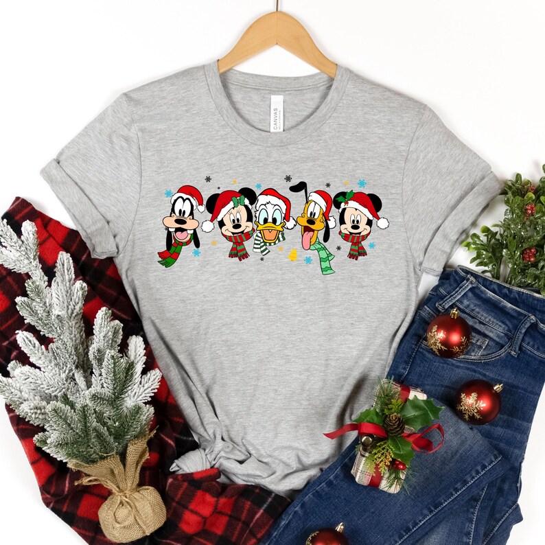 May include: A gray t-shirt with a Christmas-themed design featuring Mickey Mouse, Minnie Mouse, Donald Duck, Goofy, and Pluto wearing Santa hats and scarves.