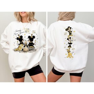 Puede incluir: Sudadera blanca con un dise&ntilde;o de A&ntilde;o Nuevo. Presenta a Mickey y Minnie Mouse con ropa formal, brindando con copas de champ&aacute;n. La parte trasera muestra a Mickey, Minnie y Pluto celebrando. El texto "Happy New Year" est&aacute; escrito en la parte delantera.