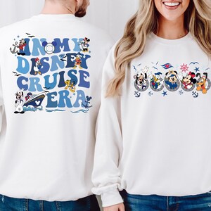 May include: White sweatshirts with a Disney Cruise themed design. One sweatshirt has the text "In My Disney Cruise Era" with a cruise ship and Disney characters. The other sweatshirt has a row of Disney characters in life preservers.